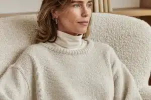 Frau Mitte 30 mit schulterlangem braunem Haar und hellem Strickpullover sitzt mit einem Buch im Bouclé-Sessel