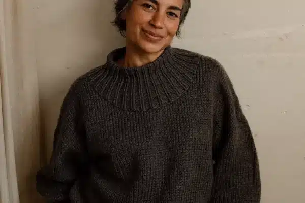 Frau um die 50 mit kurzem grau meliertem Haar und dunklem Strickpullover lehnt lächelnd an einer Betonwand