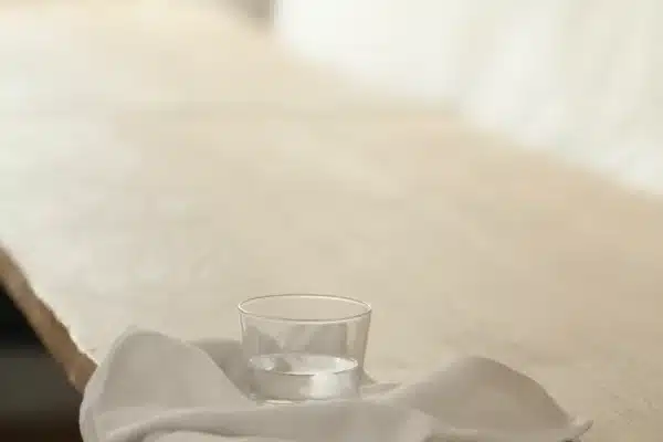 Wasserglas auf einer locker drapierten Leinenserviette an der Kante eines hellen Eichentischs im Tageslicht