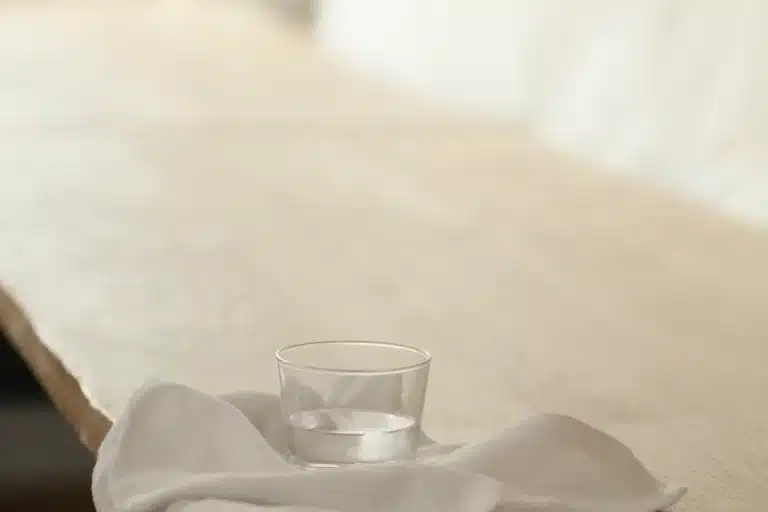 Wasserglas auf einer locker drapierten Leinenserviette an der Kante eines hellen Eichentischs im Tageslicht