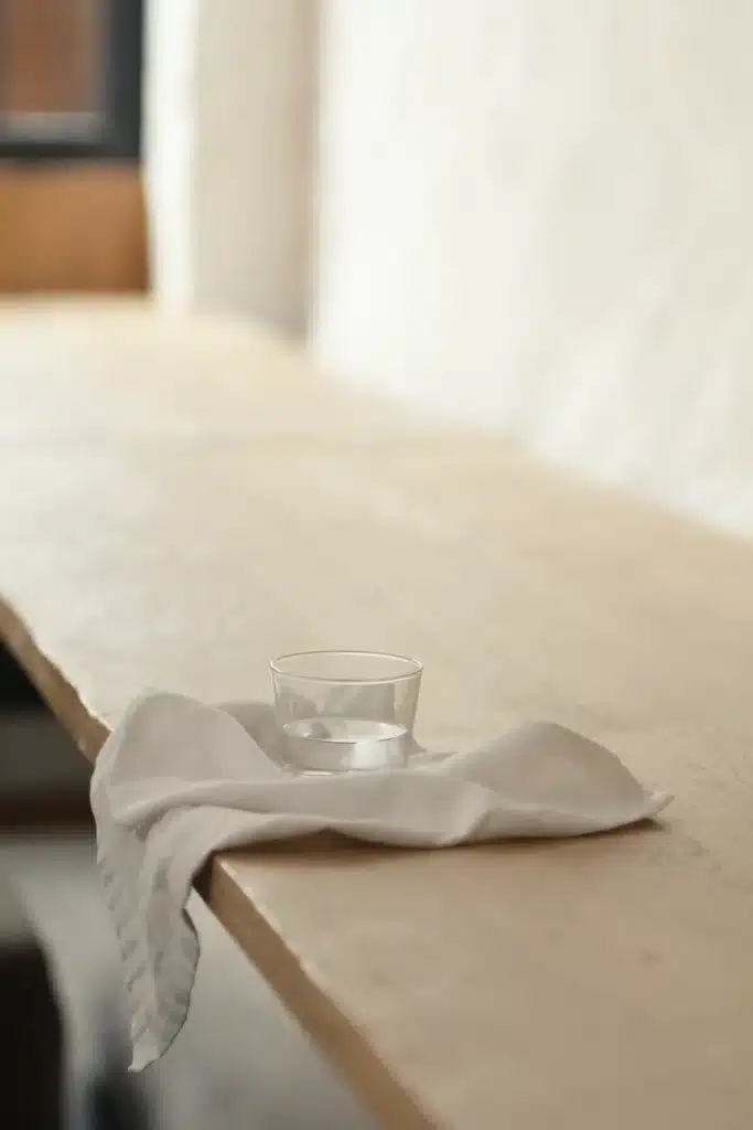 Wasserglas auf einer locker drapierten Leinenserviette an der Kante eines hellen Eichentischs im Tageslicht